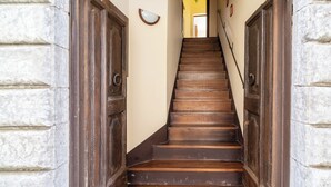 Un escalier en bois muni d’une rampe, flanqué de murs en pierre et de portes en bois.