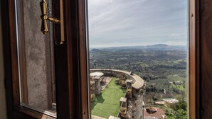 Une vue depuis une fenêtre d’une pièce donnant sur une pelouse verdoyante et des constructions en pierre.