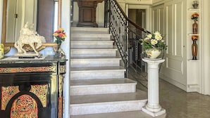 A grand staircase with white walls and a marble floor, leading to a landing with a mirror and a statue. - Hssoverato (Soverato)