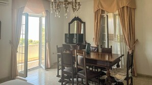 A hotel room with a dining table, chairs, a chandelier, a television, and a balcony with curtains. - Hssoverato (Soverato)