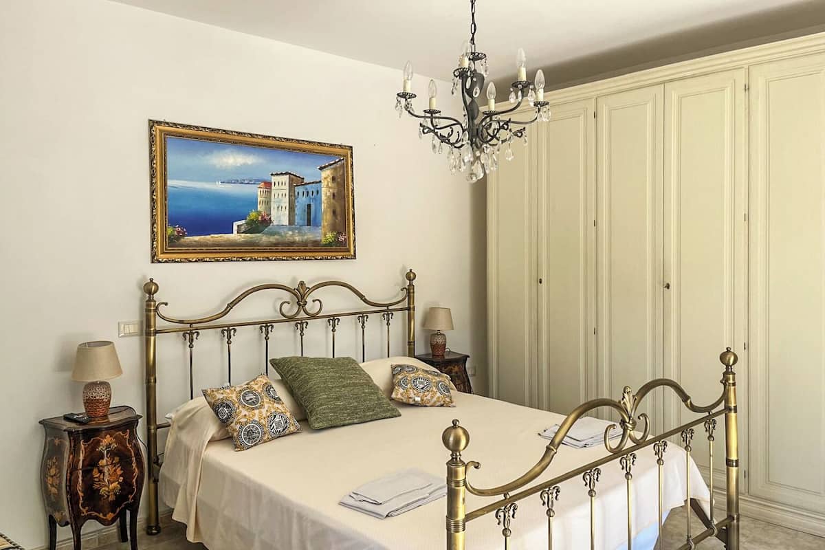 Ein ordentlich eingerichtetes Schlafzimmer mit Bett, Nachttischen, einer Chandelüster, einem Gemälde und einem Kleiderschrank.