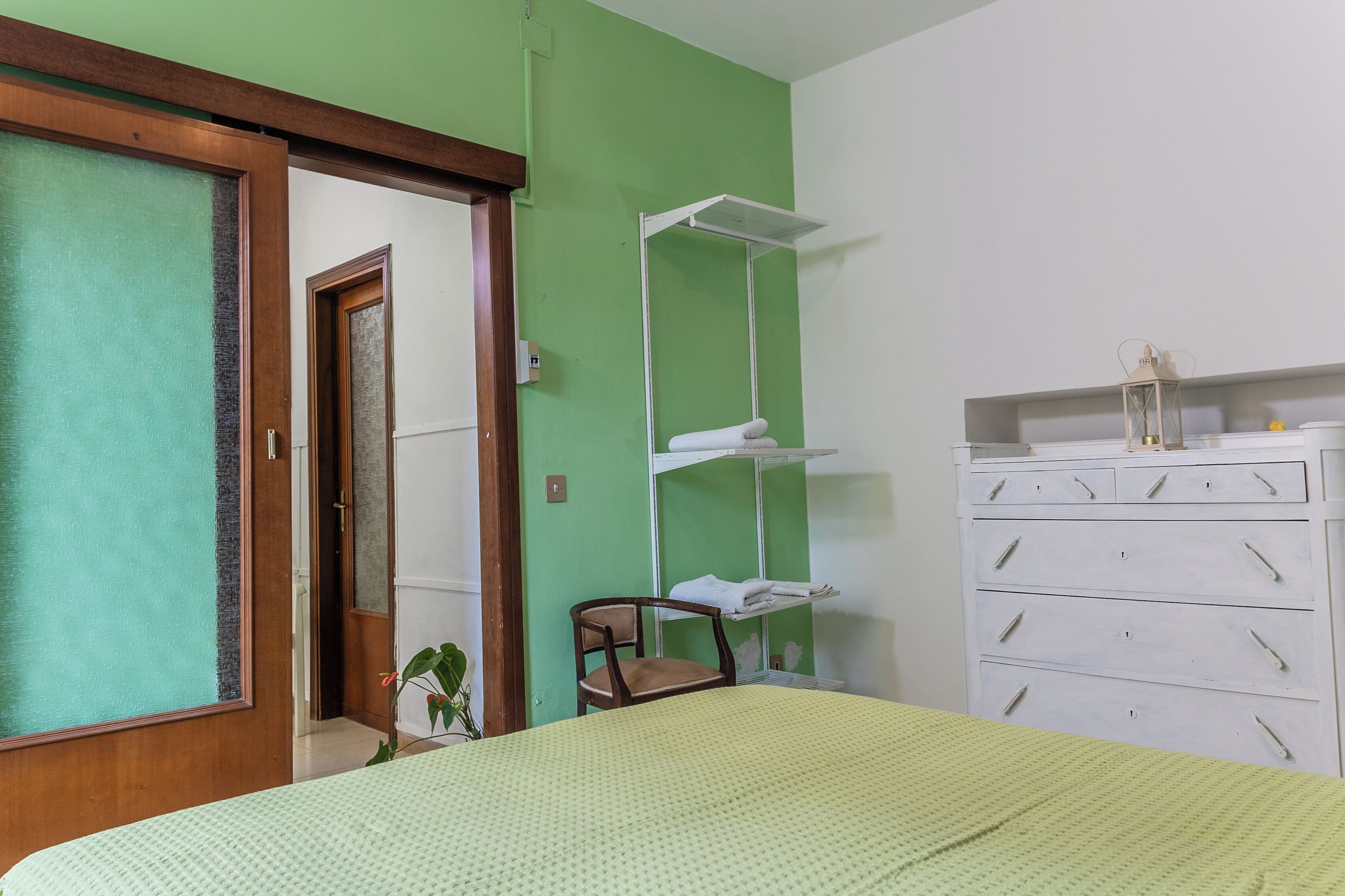 A room with a bed, a chair, a dresser, and a shelf unit.
