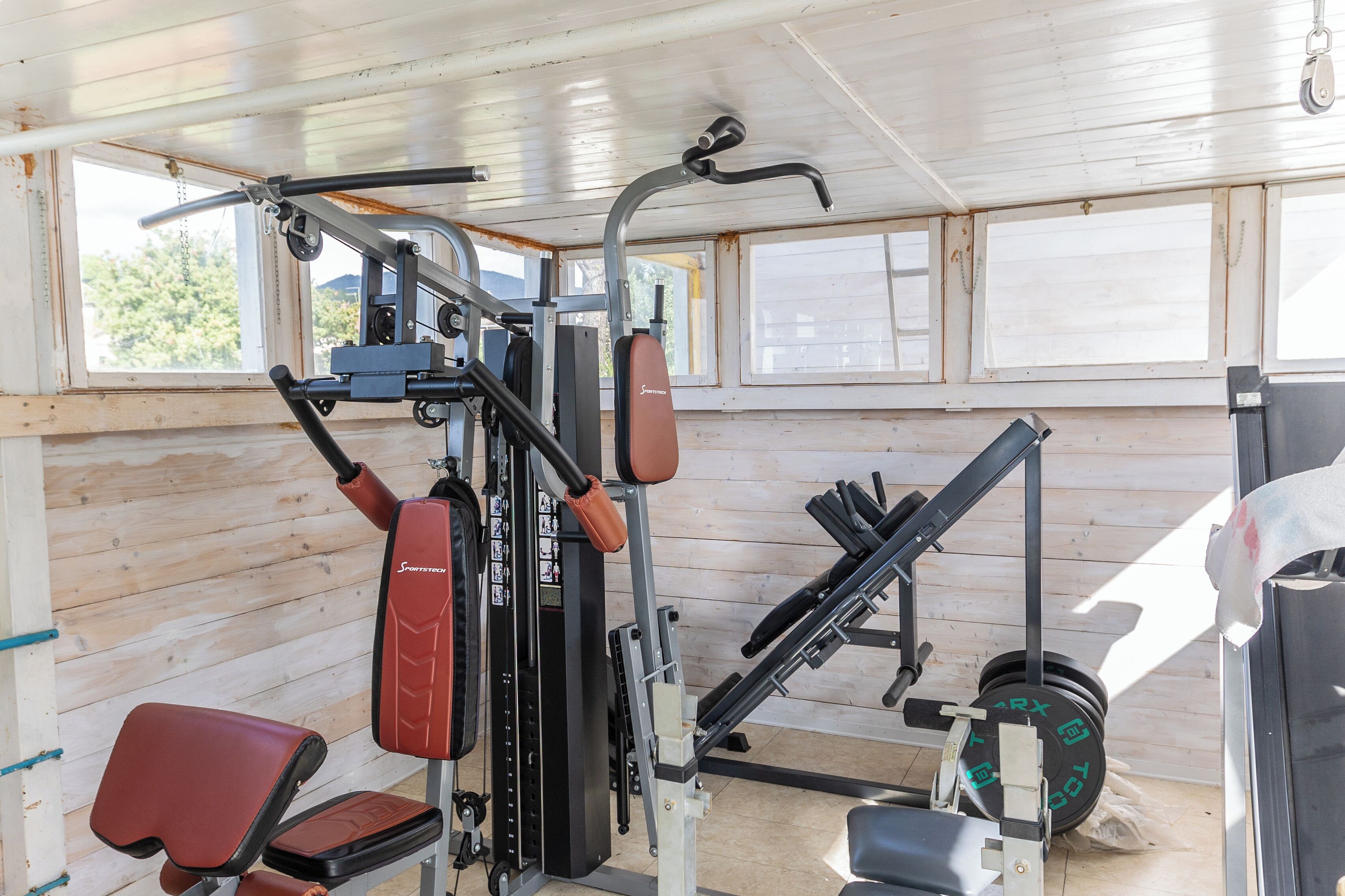 Een sportschool met diverse fitnessapparaten, waaronder een bank, krachttoestellen en een squatrek.