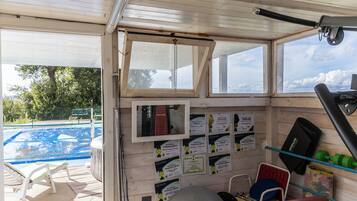 A room with a view of a swimming pool, exercise equipment, and informational cards on the wall.