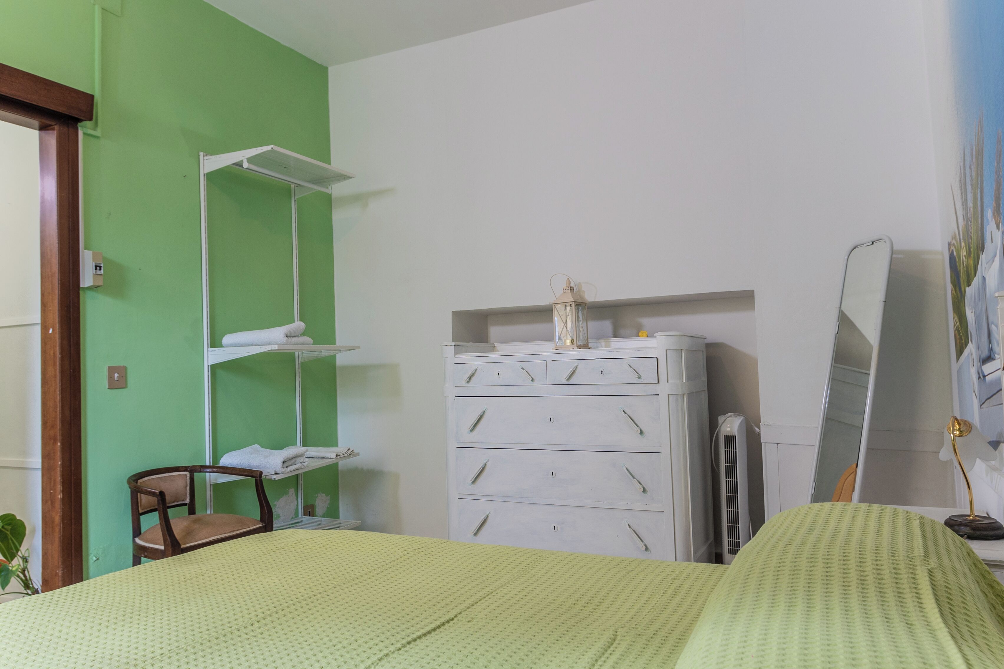A bedroom with a bed, a dresser, a chair, a mirror, and a radiator.