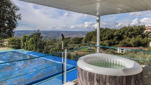 Un espace extérieur abrité comprenant un jacuzzi, une piscine bleue et une vue sur un paysage lointain.