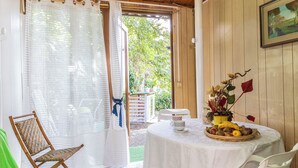 Une pièce avec un plafond en bois, une table blanche sur laquelle se trouve un panier de fruits, une chaise en osier et une chaise blanche.