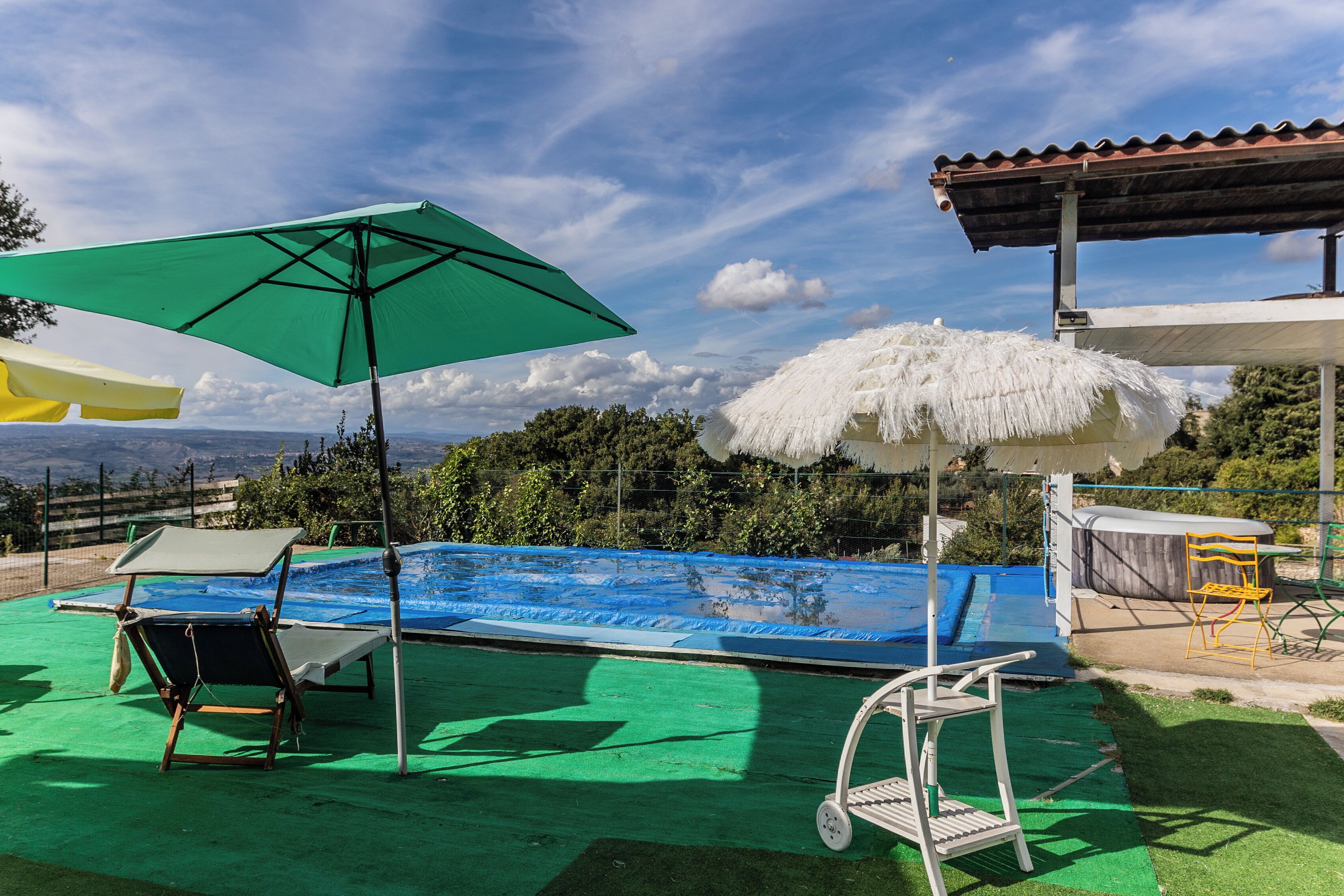 Una piscina con una cubierta verde, una sombrilla blanca y una estructura de techo de paja blanca.
