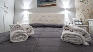 Cama bem arrumada com um edredom cinza e duas toalhas enroladas ao lado.