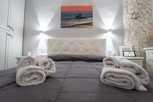 Un letto rifatto con un patchwork grigio e due asciugamani arrotolati di lato.