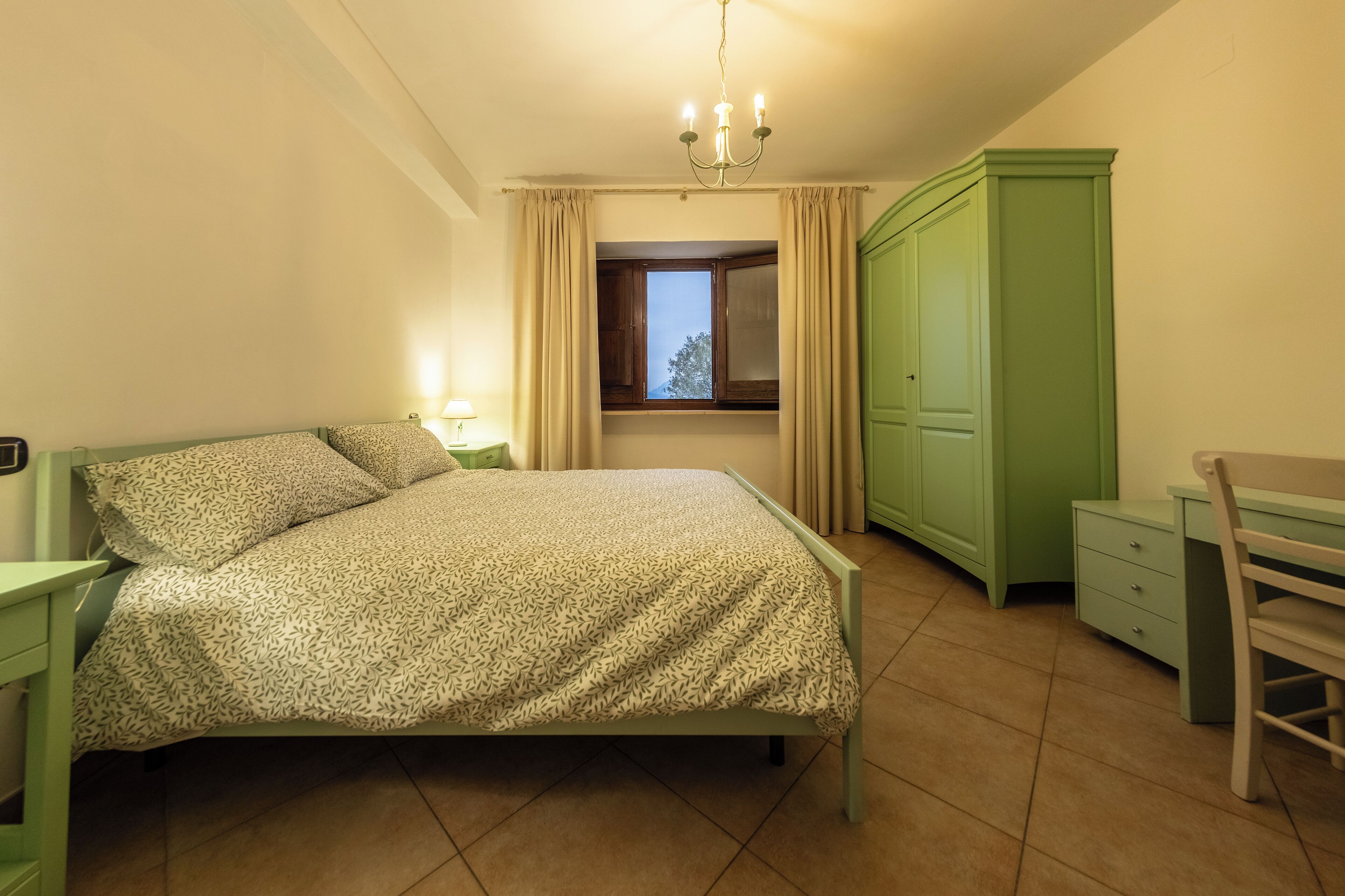 A bedroom with a bed, a desk, a wardrobe, and a window with curtains.