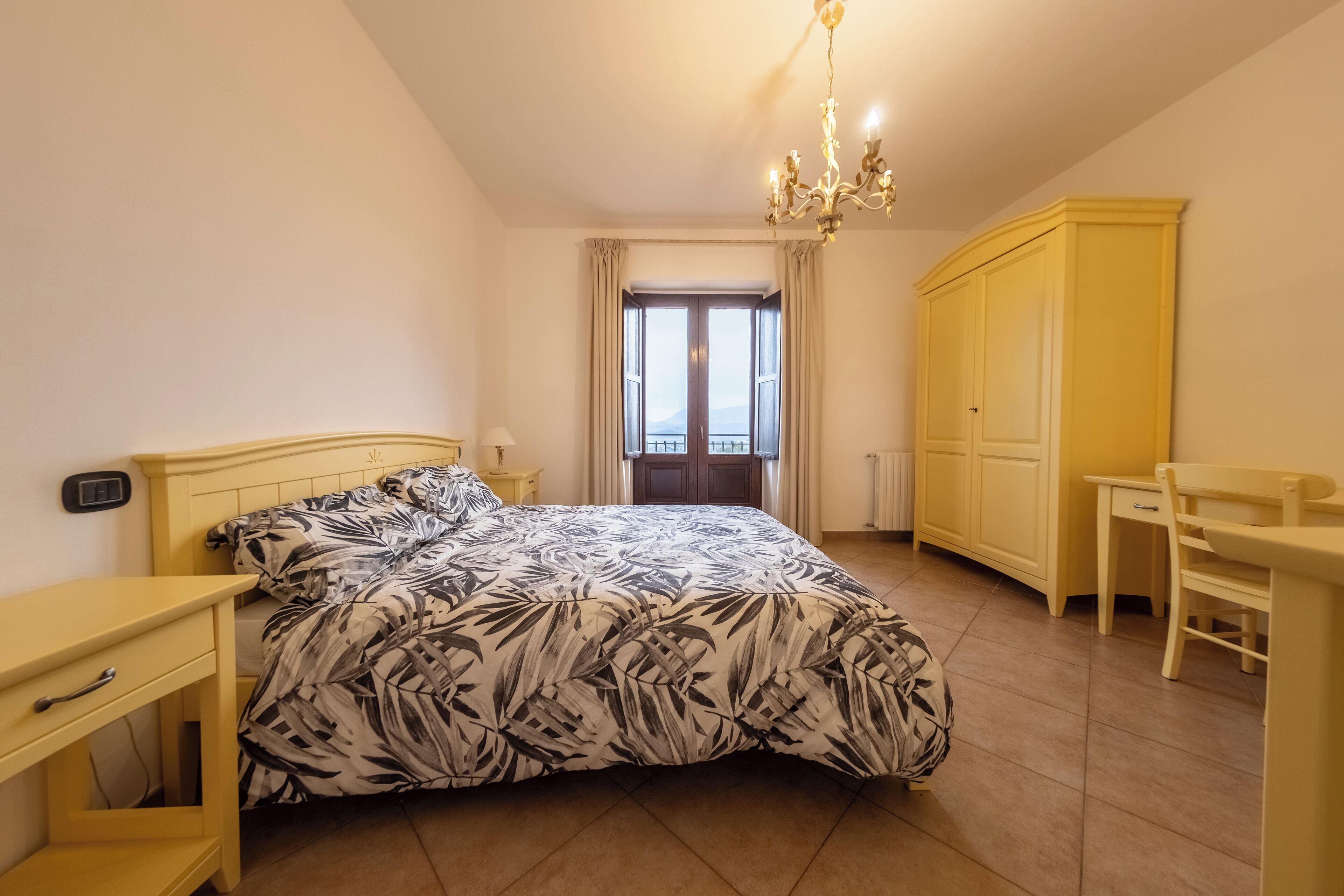 A bedroom with a bed, a desk, a chair, a wardrobe, and a window with curtains.