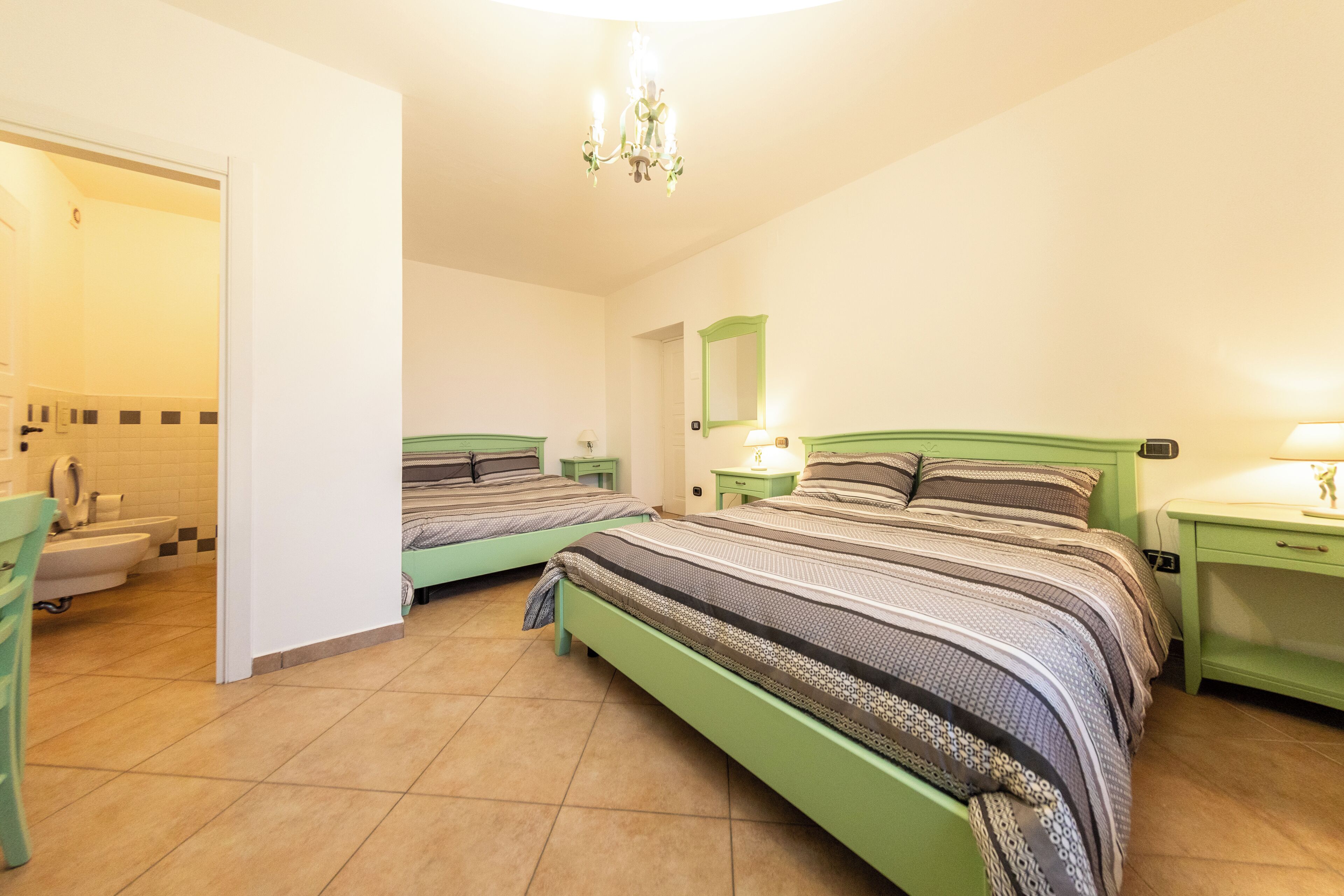 Une chambre à coucher avec deux lits verts, une salle de bain avec un lavabo blanc et une baignoire, et un lustre.