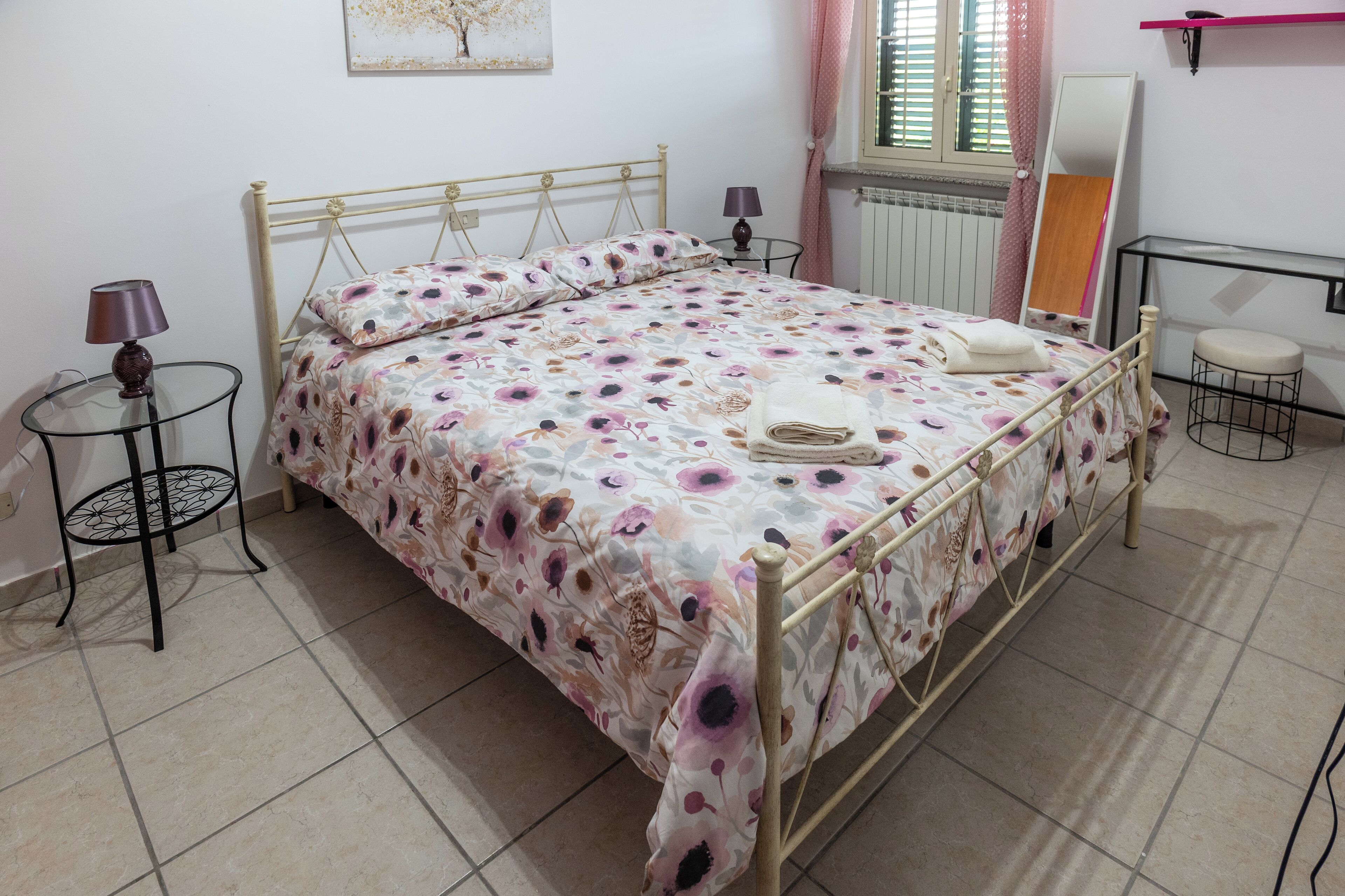 Una cama bien hecha con una colcha estampada, una mesita de noche con una lámpara y un taburete pequeño.