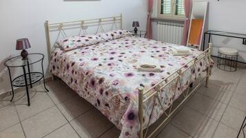 Una cama bien hecha con una colcha estampada, una mesita de noche con una lámpara y un taburete pequeño.