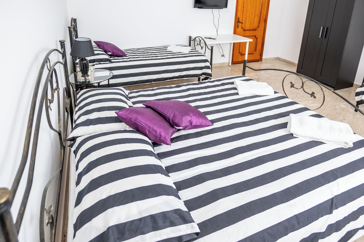 Une chambre d’hôtel avec deux lits, chacun agrémenté de draps à rayures et d’oreillers violets. On y trouve une petite table avec une lampe, un téléviseur fixé au mur et une armoire.