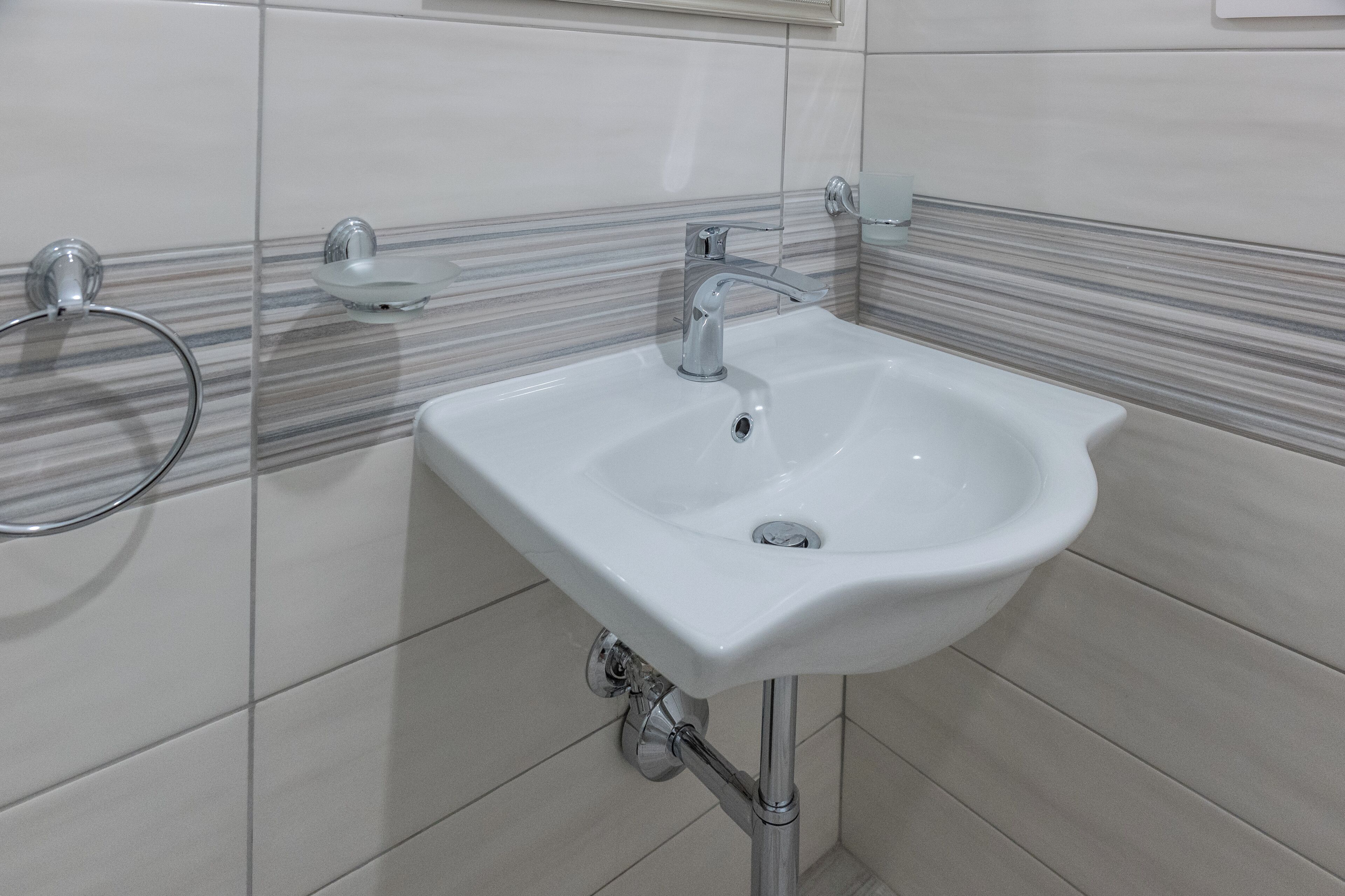 A bathroom with a white sink, chrome faucet, and towel rack.