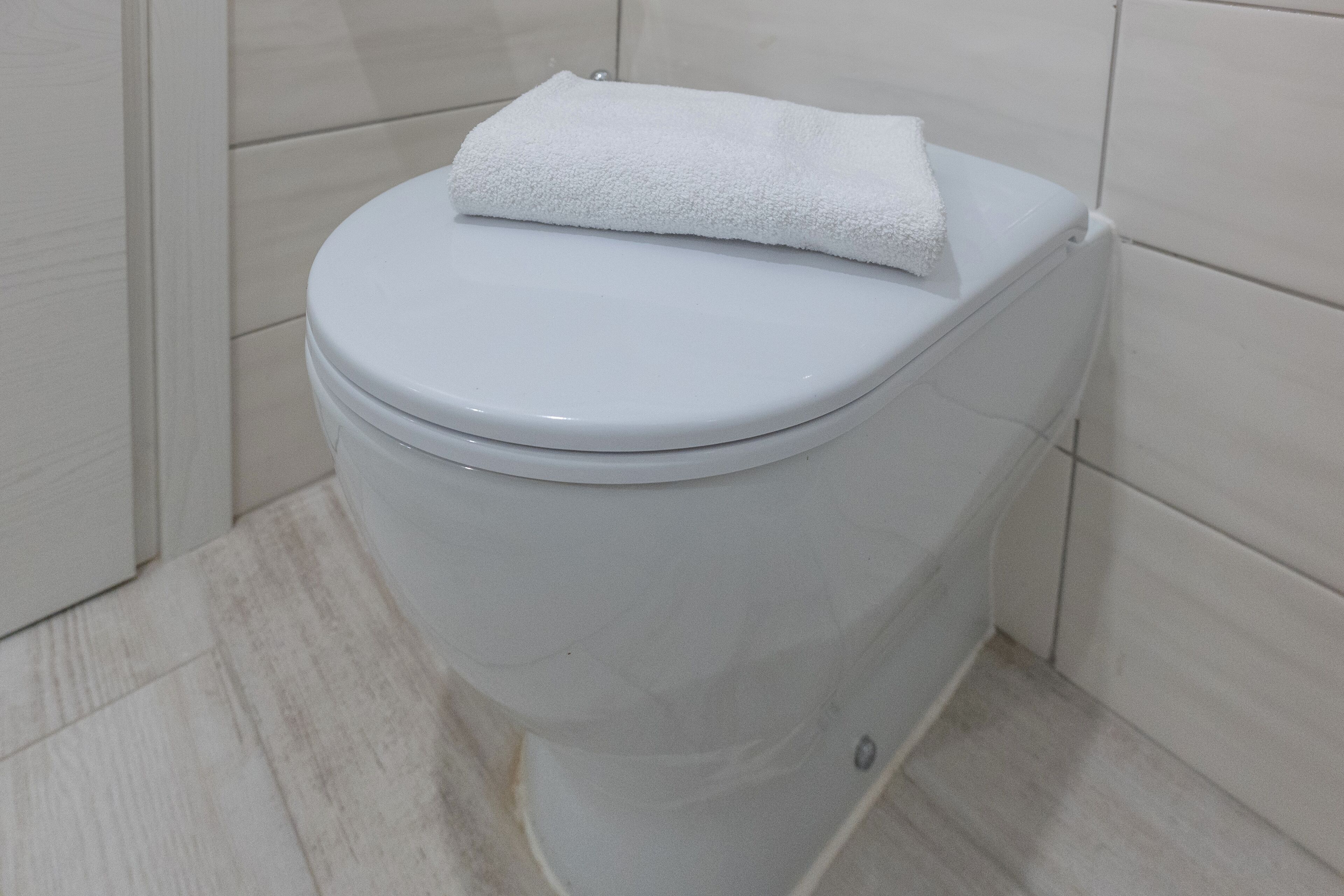 A white toilet with a white towel on top, located in a bathroom with light-colored tiles.