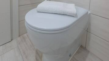A white toilet with a white towel on top, located in a bathroom with light-colored tiles.