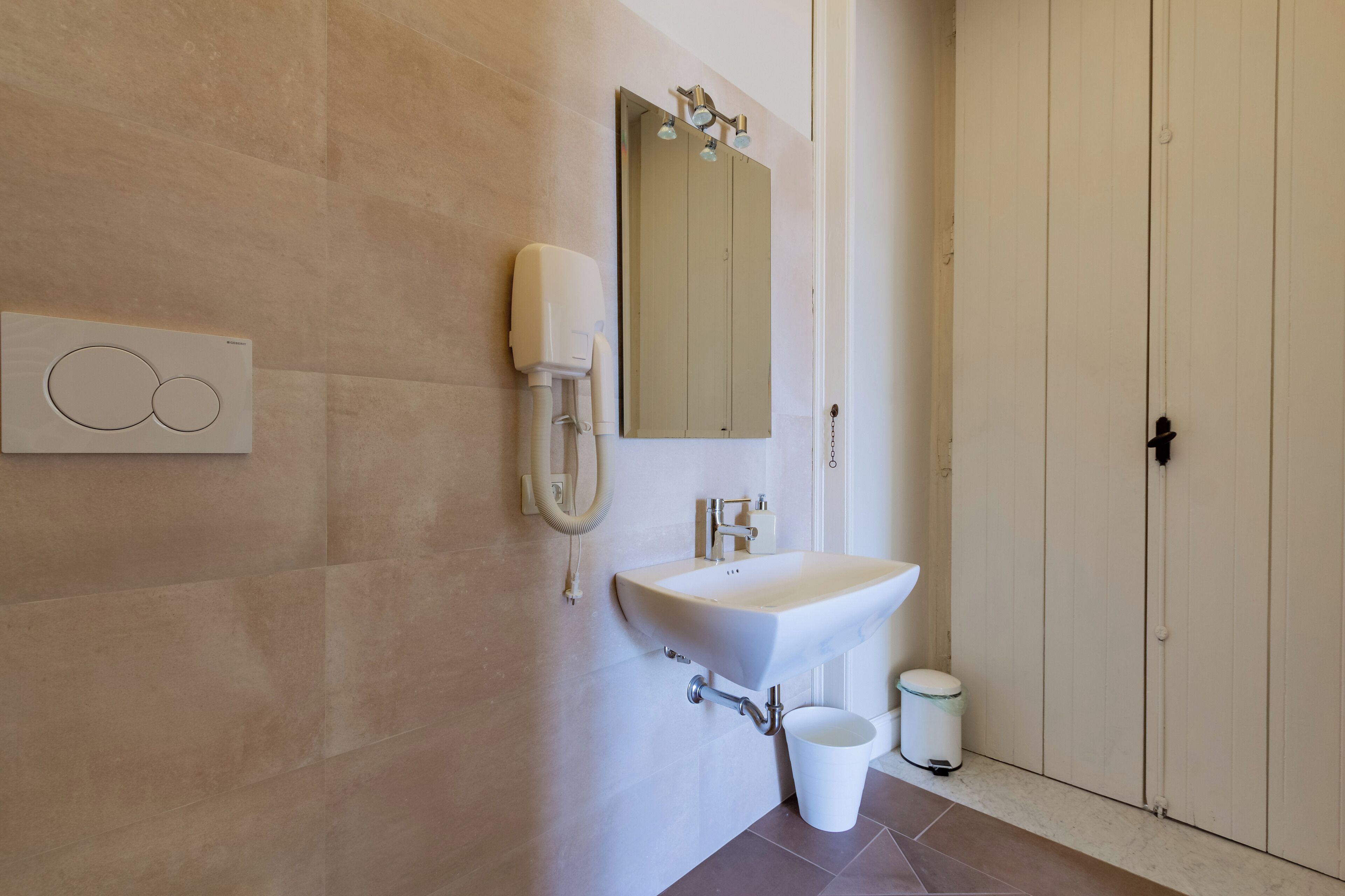 Un baño moderno con un lavamanos blanco, un espejo y un dispensador de toallas.