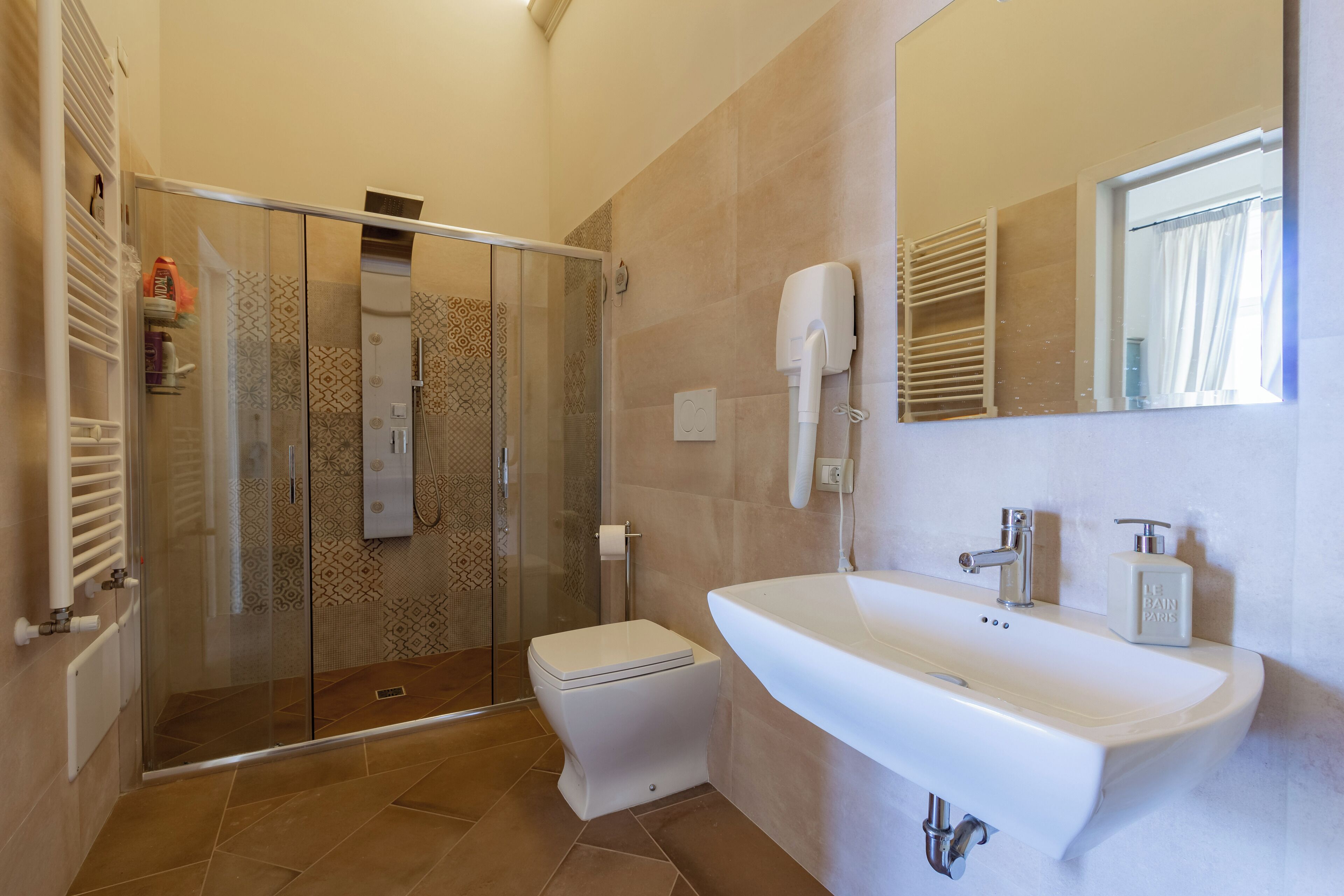 Un baño moderno con cabina de ducha de vidrio, inodoro blanco, lavabo grande con espejo y un perchero para toallas.