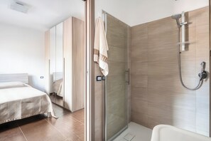 Un baño moderno con ducha, puerta de cristal y cama con colcha estampada.