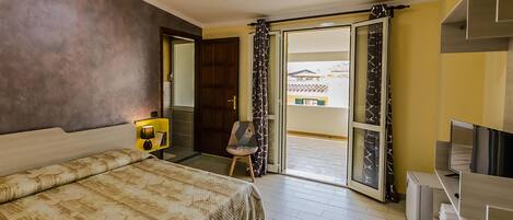 A hotel room with a bed, a TV, a desk, and a balcony with a view of buildings.