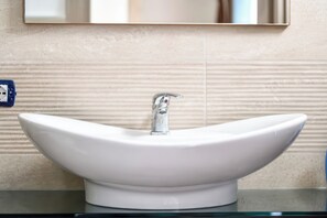 Un lavabo blanco con un grifo moderno, instalado sobre una encimera de cristal frente a una pared con textura.
