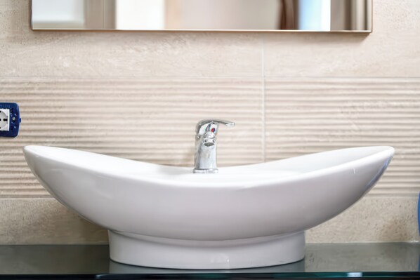 A white vessel sink with a modern faucet, mounted on a glass countertop against a textured wall. - B&B AniMo (Loceri)