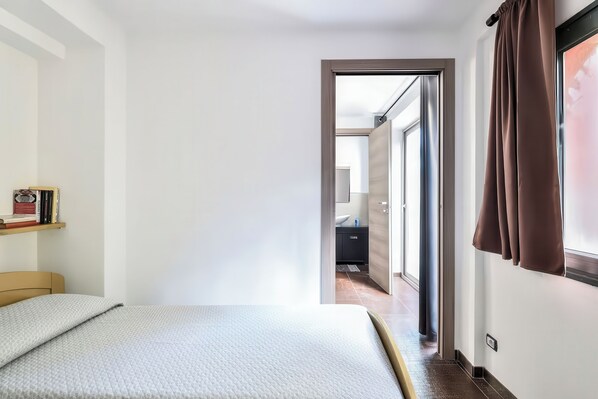 Une chambre à coucher avec un lit, une table de chevet, une étagère remplie de livres et une vue sur la salle de bain.