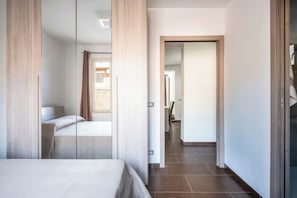 Ett modernt hotellrum med en stor säng, en spegel och utsikt över korridoren.