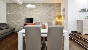 A modern living room with a dining table, grey chairs, a sofa, a TV, and a decorative glass dome. - B&B AniMo (Loceri)