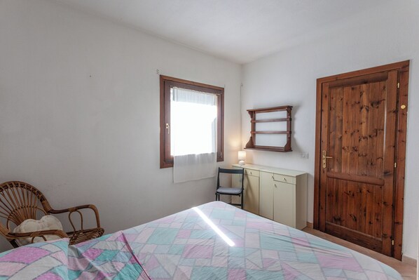 Une chambre à coucher comprenant un lit, une chaise, un bureau, une armoire et une fenêtre.