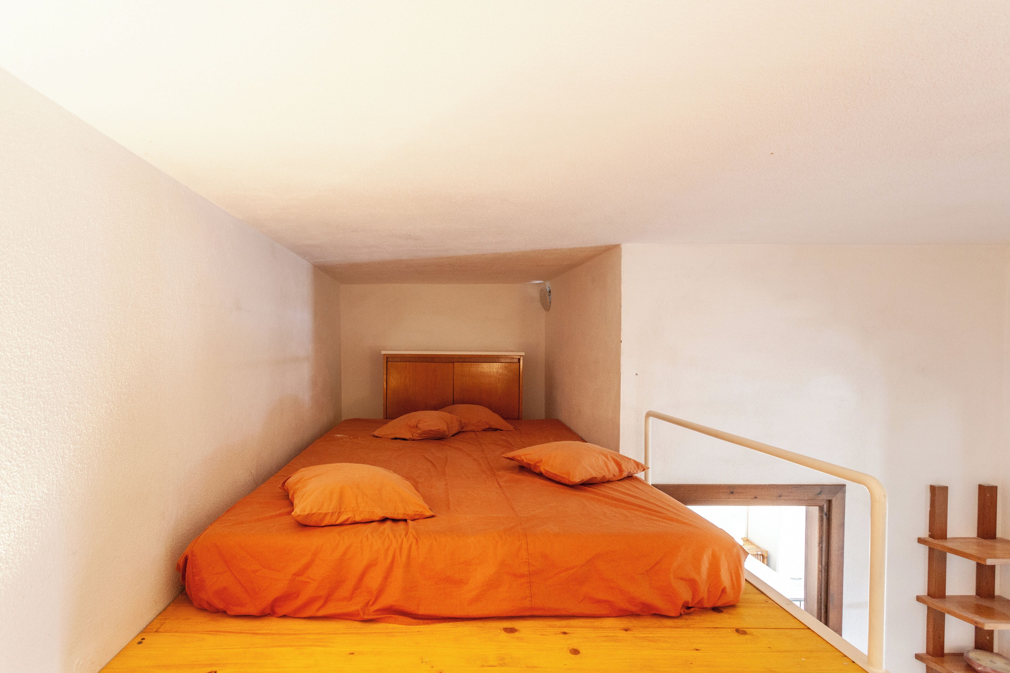 A small, narrow room with a single bed, a wooden headboard, and a window with a view.