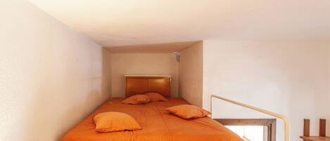 A small, narrow room with a single bed, a wooden headboard, and a window with a view.