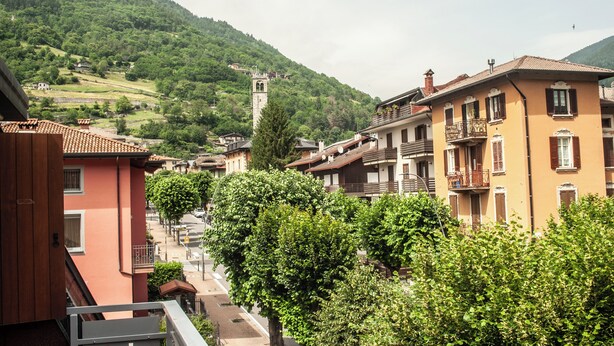 A hillside town with traditional buildings, a prominent tower, and lush greenery. - Appartamento Edolo, Bilocale & Monolocale (Edolo)