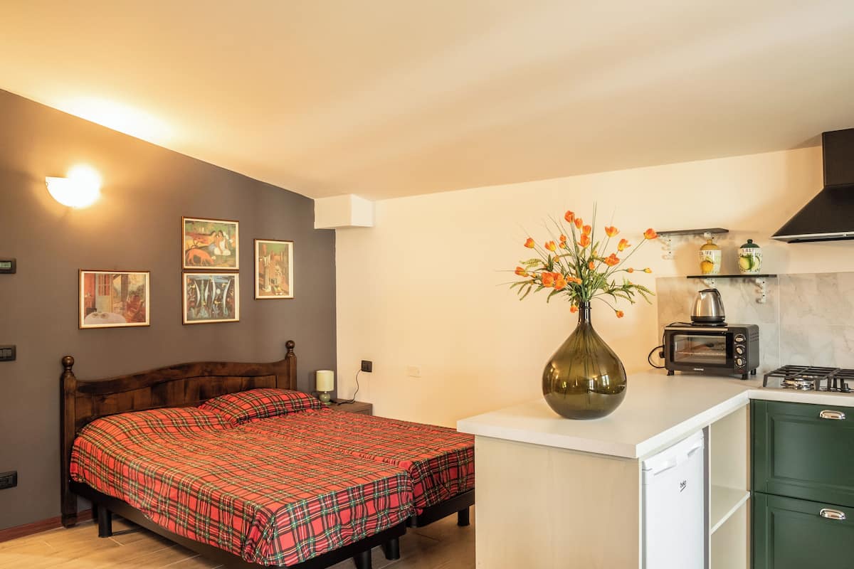 A bedroom with a bed, a nightstand, a lamp, and a wall-mounted shelf with a vase of flowers.