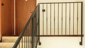 A staircase with a black metal railing, wooden steps, and a brass vase on the landing. - Appartamento Edolo, Bilocale & Monolocale (Edolo)