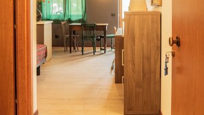 A hallway with wooden flooring, a dining area with a table and chairs, and a small kitchenette area. - Appartamento Edolo, Bilocale & Monolocale (Edolo)