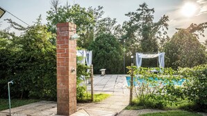 Un pilar de ladrillo, una piscina y un espacio cubierto con una pérgola.