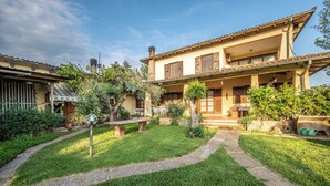 Una casa de dos pisos con un patio, un sendero de piedra y diversas plantas.