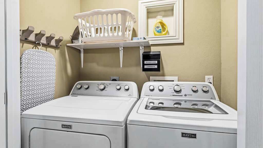 A laundry room with two Maytag washers and dryers, a drying rack, and a shelf with a detergent bottle.