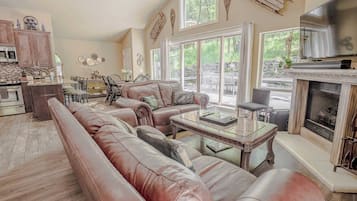 Uma sala de estar ampla com um sofá de couro grande, lareira e área de jantar com vista para o exterior.