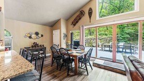Un espace repas avec une grande table et des chaises, un coin cuisine doté d’un plan de travail en granit, et une vue sur l’extérieur grâce à de grandes portes-fenêtres coulissantes.