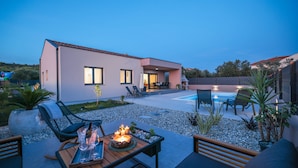 Ein modernes Haus mit Schwimmbad, Sitzgelegenheiten im Freien und einer Terrassenfläche.