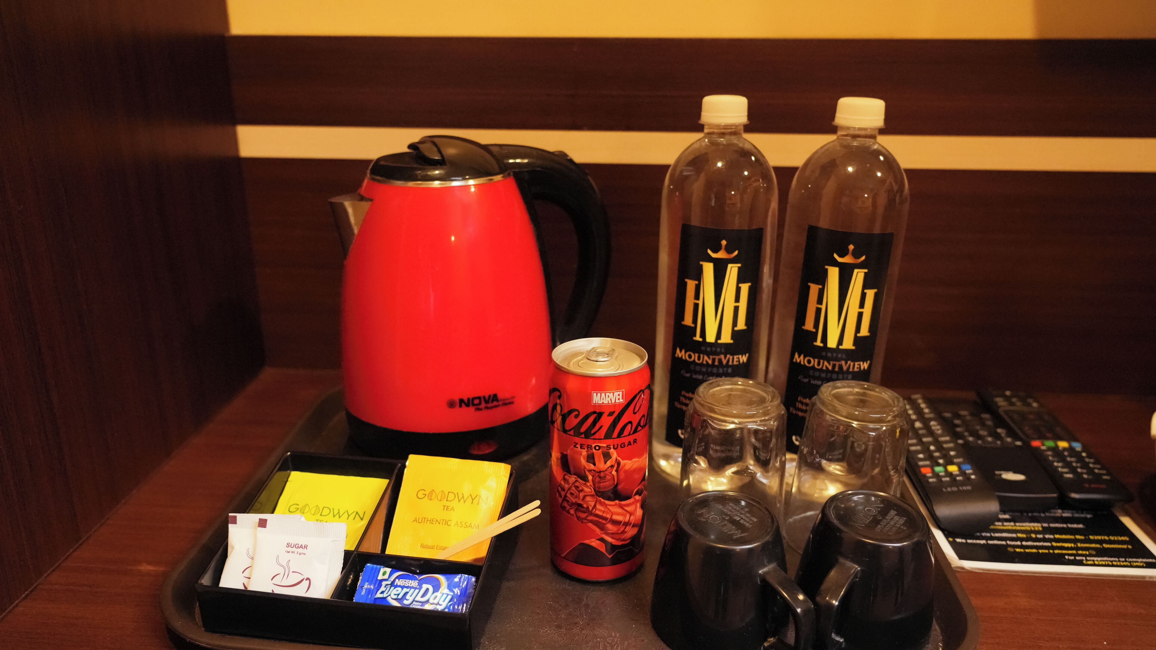 Hotellin minibaarissa on punainen sähköinen vedenkeitin, kaksi pulloa Mountview-hotellin alkoholipitoista juomaa, tölkki Coca-Cola Zero Sugar -limsaa, paketti Nestle EveryDay -teetä sekä tarjotinalusta, jossa on sokeripaketteja ja paketti pikakahvia.