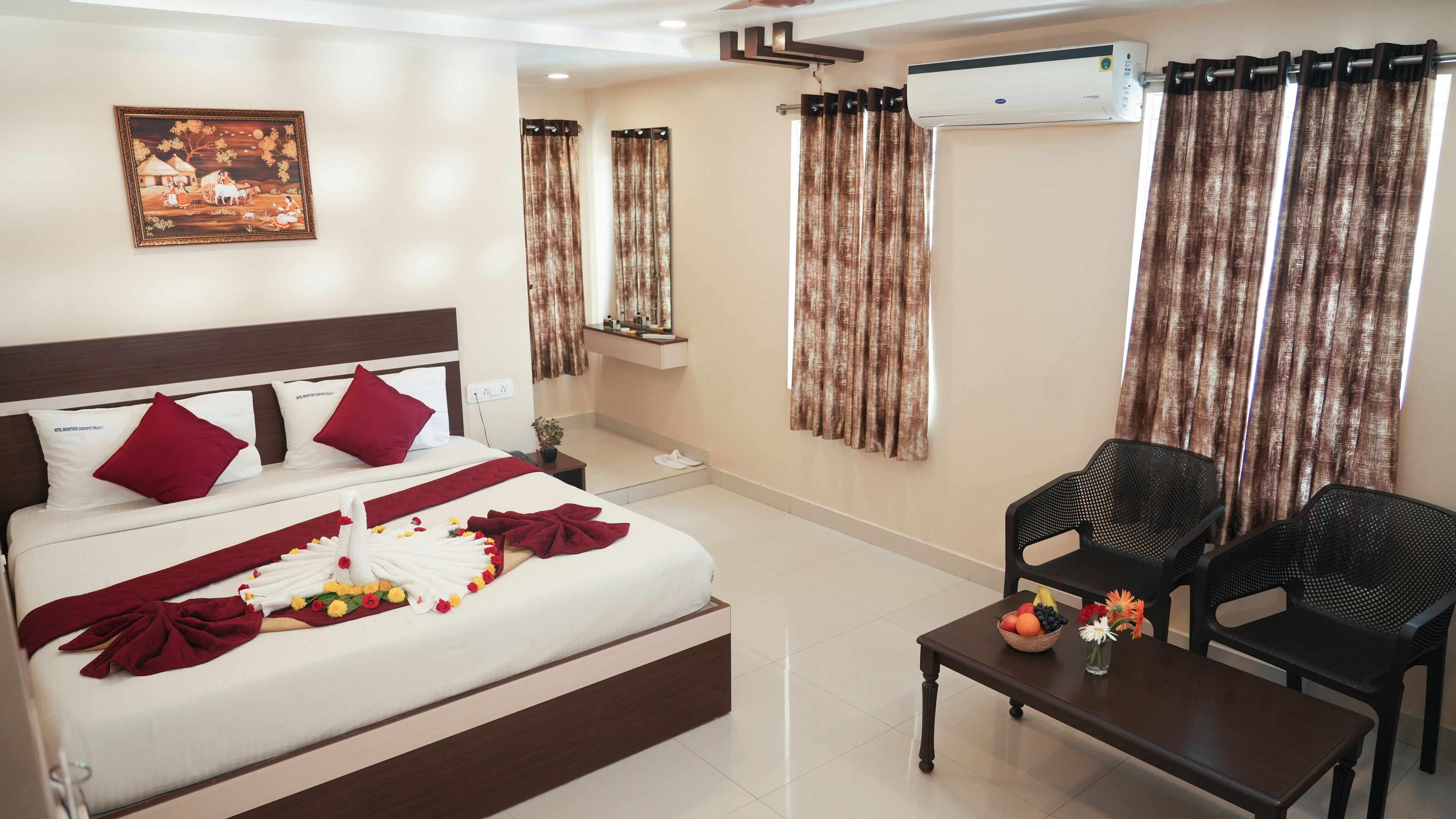 A hotel room with a bed, a desk, two chairs, a wall-mounted air conditioner, and a painting.