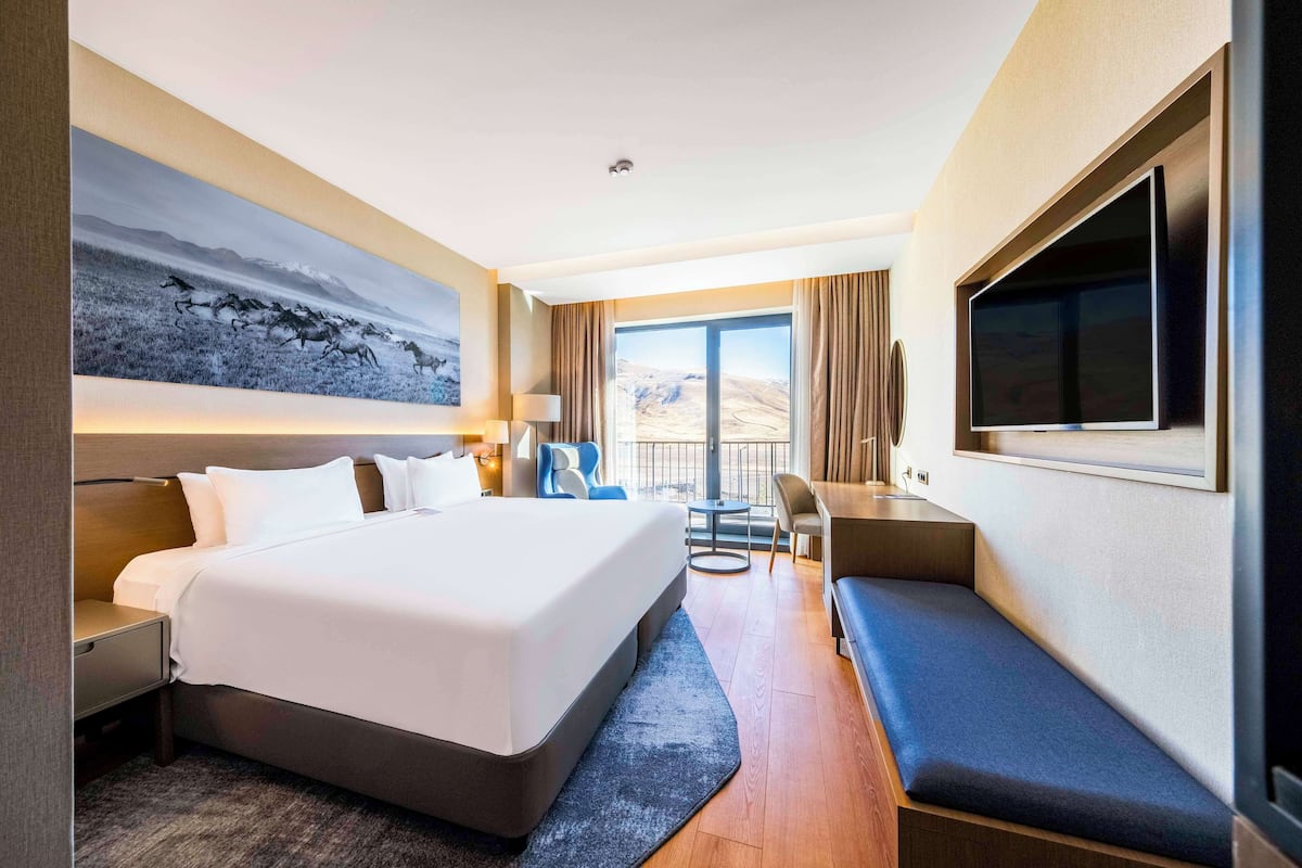 Une chambre d’hôtel moderne dotée d’un grand lit, d’un bureau, d’un coin salon et offrant une vue sur les montagnes.