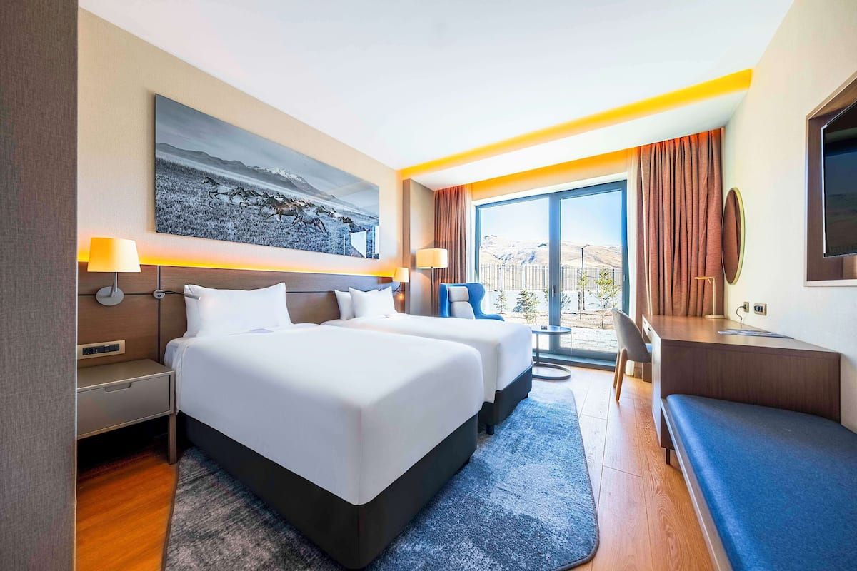 Une chambre d’hôtel moderne avec deux lits, un bureau, une chaise et une grande fenêtre donnant sur un beau paysage.
