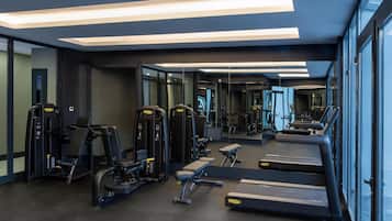 Un gimnasio moderno con diverso equipamiento de ejercicio, incluyendo cintas de correr y máquinas de pesas, y amplias ventanas que proporcionan luz natural.